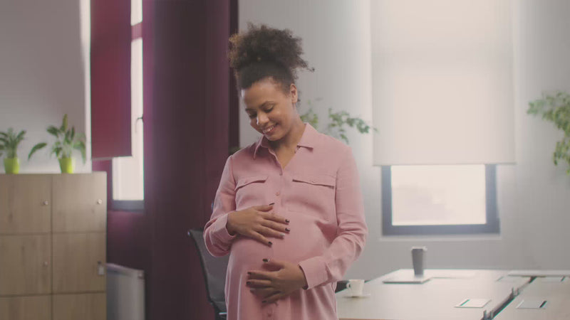 Zwangere vrouw die zachtjes haar buik aanraakt terwijl ze het full body Momie zwangerschapskussen gebruikt voor ondersteuning en comfort.